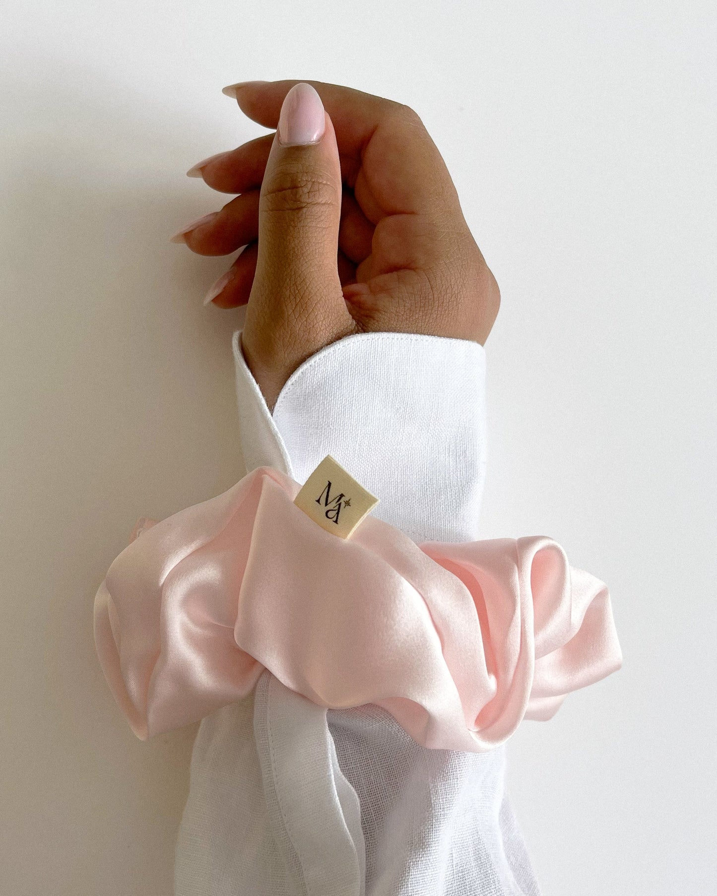 Close-up of a hand wearing a pink silk scrunchie on a white shirt