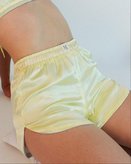 Yellow silk shorts worn by a person on a white background