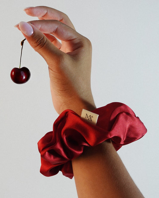 Hand wearing a red silk scrunchie holding a cherry