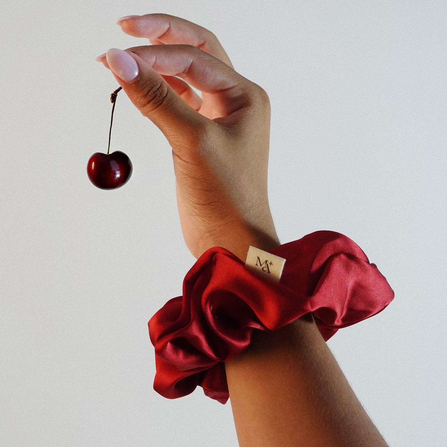 Hand wearing a red silk scrunchie holding a cherry