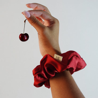 Hand wearing a red silk scrunchie holding a cherry