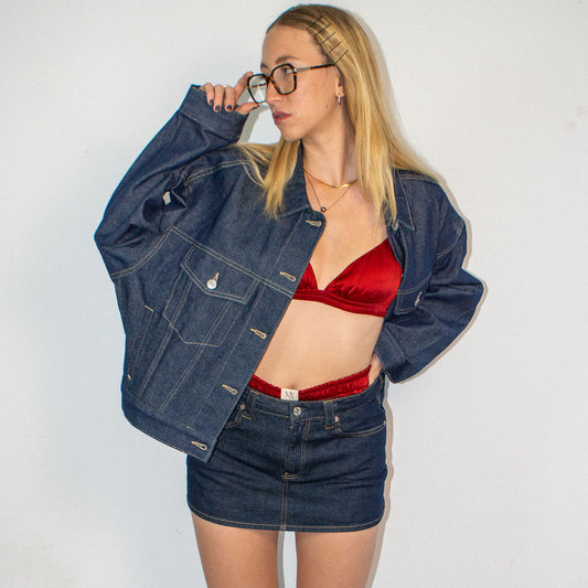 Person wearing a denim jacket over a red silk bralette and silk shorts.
