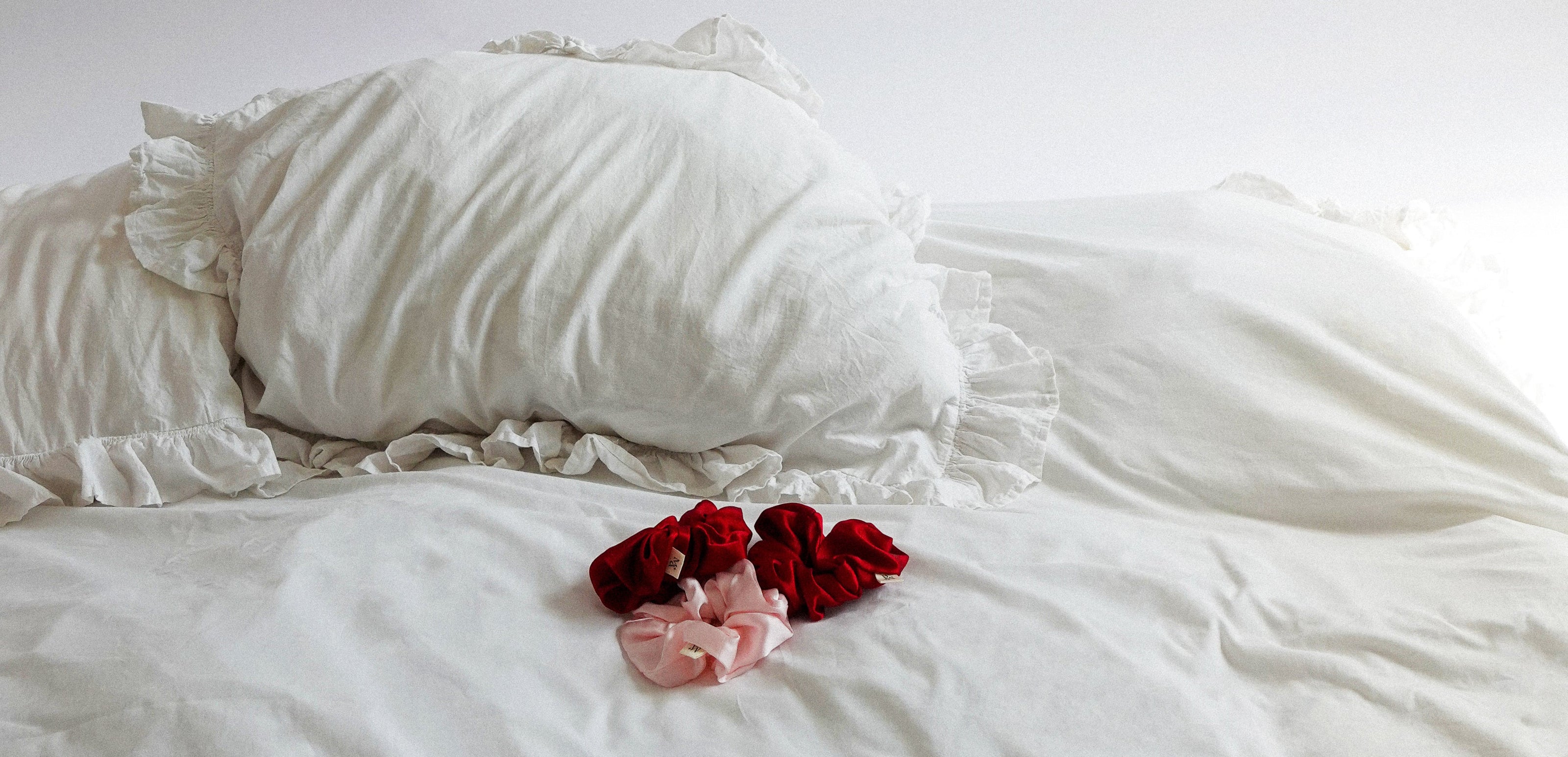 White pillows and bedding with red and pink silk scrunchies on a white background