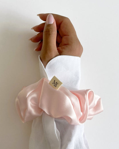 Close-up of a hand wearing a pink silk scrunchie on a white shirt