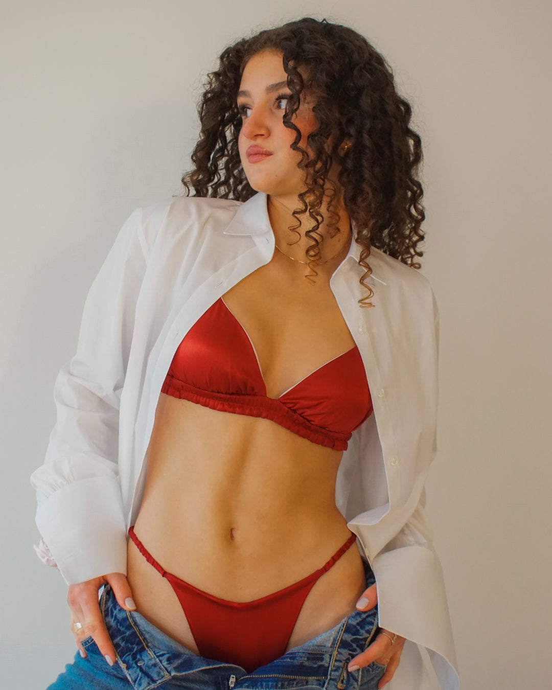 Woman wearing a silk set: red bralette and matching thong, styled with an oversized shirt and jeans.