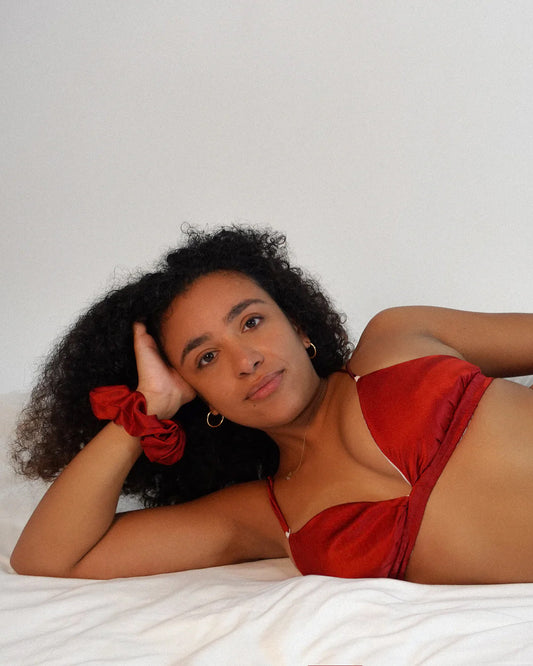 red silk bralette worn by a woman on a bed