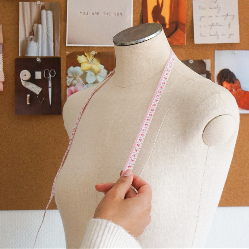 Mannequin with measuring tape against a corkboard with colorful images and notes.