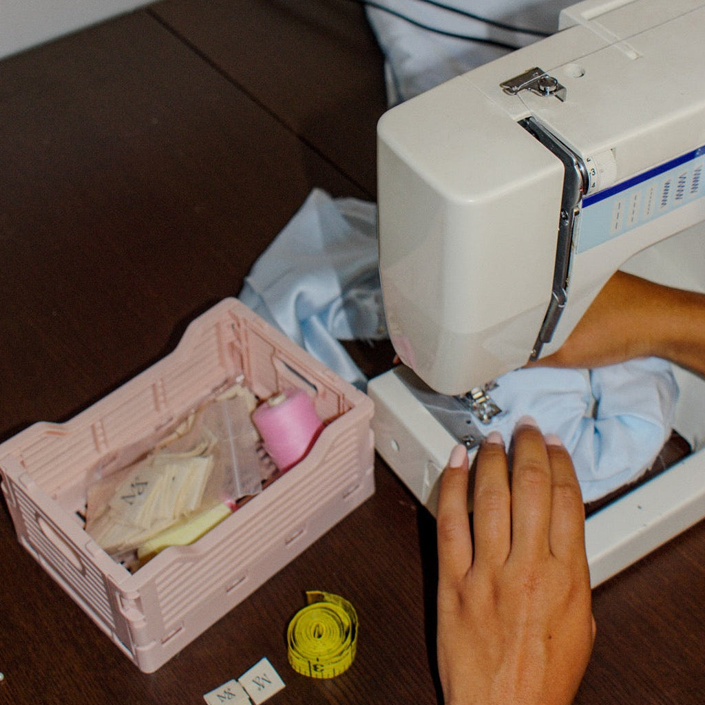 Sewing machine on a table with a pink basket of sewing supplies and a person's hand.