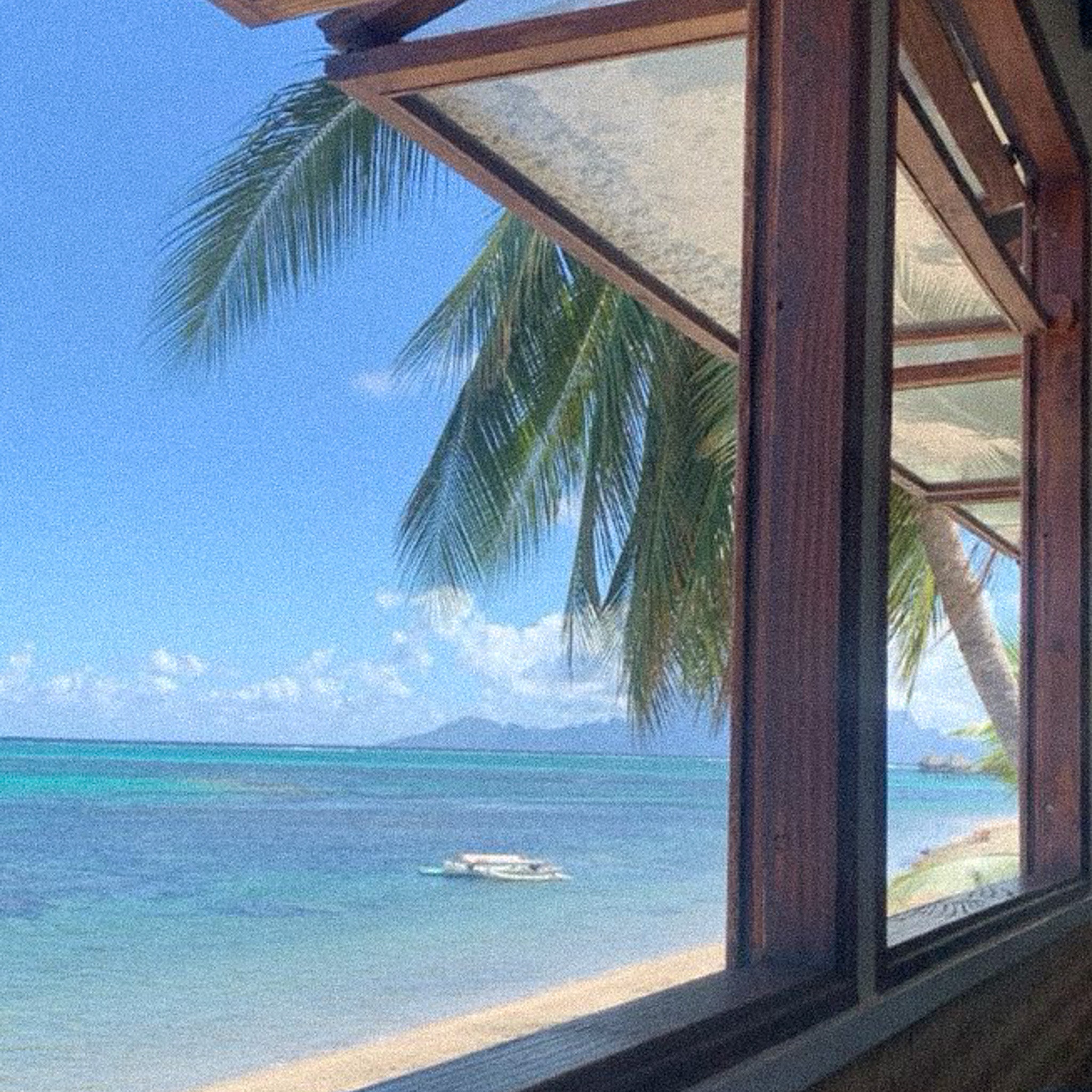 View of Tahitian beach and Moorea through a wooden window, with turquoise sea in the background.